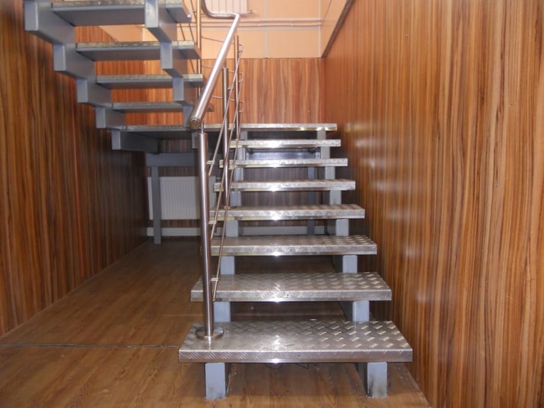 Modern metal staircase with wooden steps in wooden interior space, featuring stainless steel railings and supports
