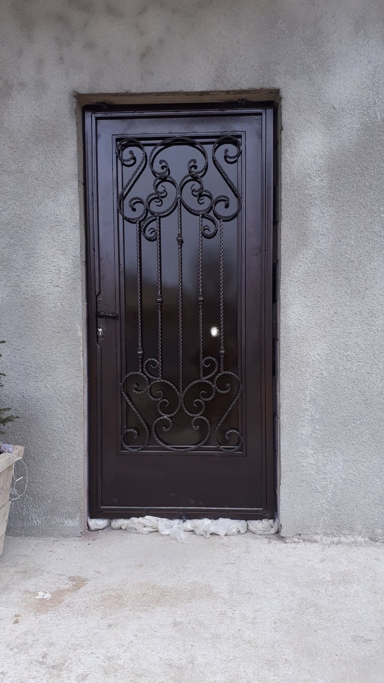 Black ornate iron security door with scrollwork design on weathered stucco wall