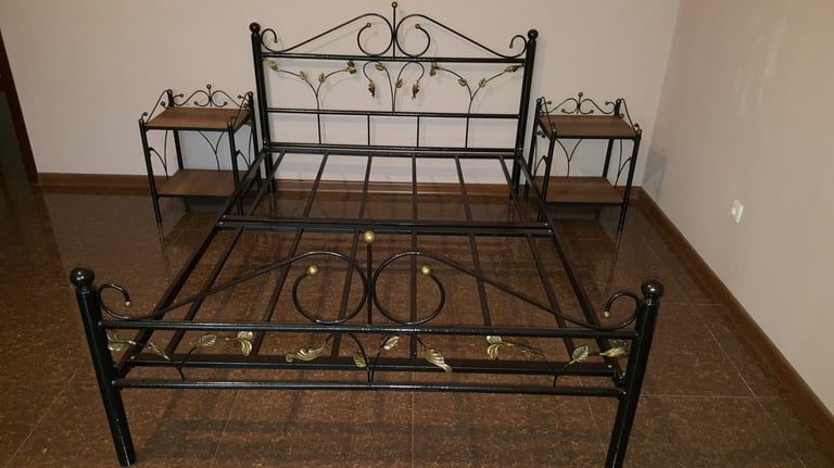 Metal bed frame with ornate black headboard and footboard, flanked by two wooden nightstands in an empty room