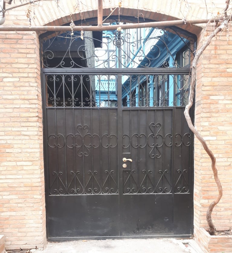 Large ornate black metal gate with decorative patterns set in a brick archway entrance