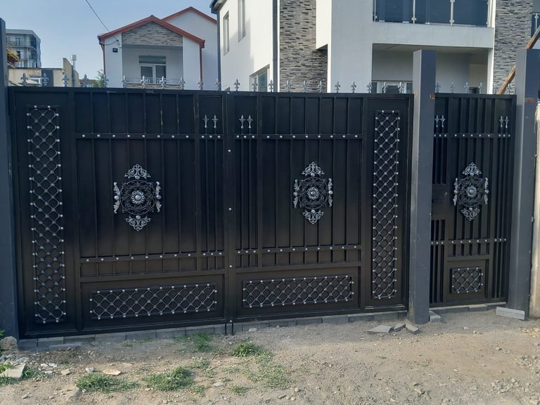 Ornate black metal driveway gate with decorative patterns and medallions in residential area