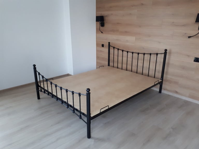 Black metal bed frame with beige mattress in a modern bedroom with wooden walls and light flooring
