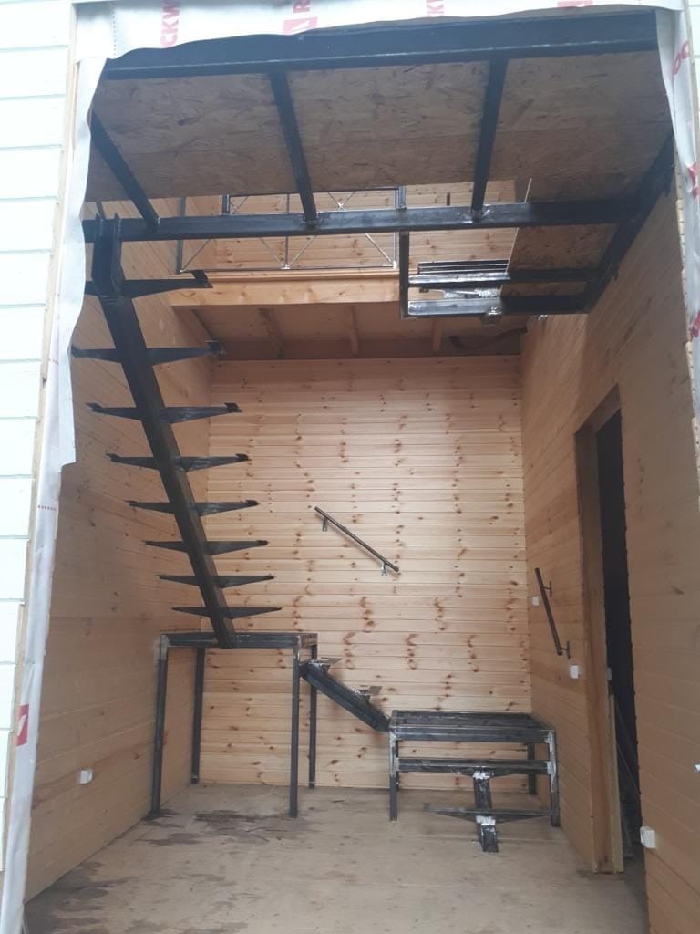 Interior of a wooden structure under construction showing exposed framing, metal beams, and wooden flooring with construction equipment