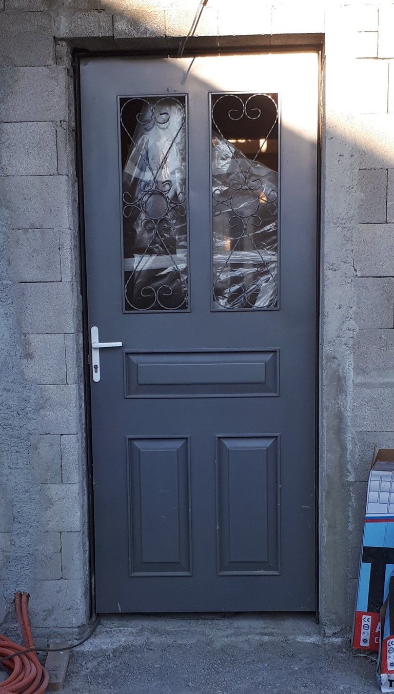 Dark blue exterior door with ornate wrought iron window panels set in a gray stone wall